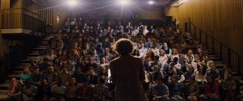 Movie still from “Denial” (2016), directed by Mick Jackson – A crowd of people sitting and standing in front of a speaker; Extreme Wide shot, High angle