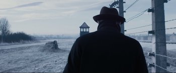 Movie still from “Denial” (2016), directed by Mick Jackson – A man wearing a hat standing in a field; Medium shot, Over the shoulder angle