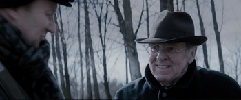 Movie still from “Denial” (2016), directed by Mick Jackson – An older man wearing glasses and a hat in a wooded area; Close Up shot, Over the shoulder angle