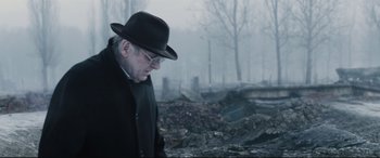 Movie still from “Denial” (2016), directed by Mick Jackson – An older man in a hat and glasses walking through a burned area; Close Up shot, Over the shoulder angle