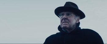 Movie still from “Denial” (2016), directed by Mick Jackson – An older man wearing glasses and a black hat; Close Up shot, Low angle