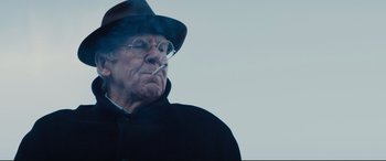 Movie still from “Denial” (2016), directed by Mick Jackson – An old man wearing a hat and smoking a cigarette; Close Up shot, Over the shoulder angle