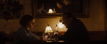 Movie still from “Denial” (2016), directed by Mick Jackson – A man and a woman sitting at a table with a bottle of alcohol; Medium shot, Over the shoulder angle