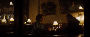 Movie still from “Denial” (2016), directed by Mick Jackson – A woman sitting at a table in front of two lamps; Wide shot, Over the shoulder angle