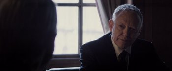 Movie still from “Denial” (2016), directed by Mick Jackson – An older man wearing a suit sitting in front of a window; Close Up shot, Over the shoulder angle