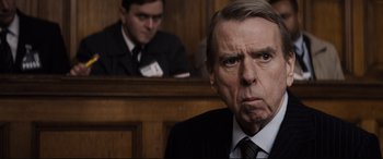 Movie still from “Denial” (2016), directed by Mick Jackson – An older man in a suit in a court room; Close Up shot, Over the shoulder angle