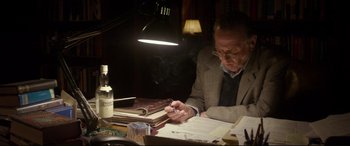 Movie still from “Denial” (2016), directed by Mick Jackson – An older man sitting at a table writing on a piece of paper; Medium shot, High angle