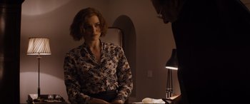 Movie still from “Denial” (2016), directed by Mick Jackson – A woman sitting in front of a lamp in a dimly - lit room; Medium shot, Over the shoulder angle