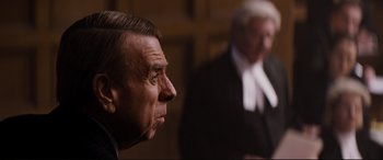 Movie still from “Denial” (2016), directed by Mick Jackson – A man in a suit and tie in front of a judge in a court room; Close Up shot, Over the shoulder angle