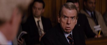 Movie still from “Denial” (2016), directed by Mick Jackson – A man in a suit and tie looking surprised at the camera; Close Up shot, Over the shoulder angle