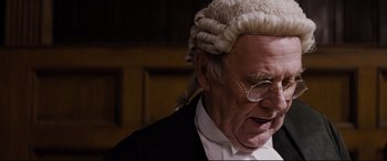 Movie still from “Denial” (2016), directed by Mick Jackson – An old man wearing a wig and glasses; Close Up shot, High angle