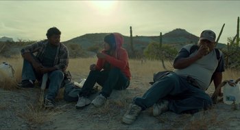 Movie still from “Desierto” (2015), directed by Jonás Cuarón – A group of people sitting on the ground in the desert; Medium shot, Low angle