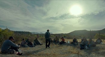 Movie still from “Desierto” (2015), directed by Jonás Cuarón – A group of people sitting in a field with a man standing in front of them; Extreme Wide shot, High angle