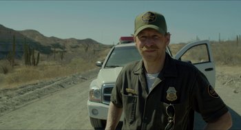 Movie still from “Desierto” (2015), directed by Jonás Cuarón – A man standing next to a white truck on the side of a dirt road; Medium shot, Over the shoulder angle