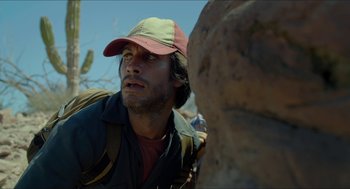 Movie still from “Desierto” (2015), directed by Jonás Cuarón – A person wearing a hat near a rock; Close Up shot, Low angle