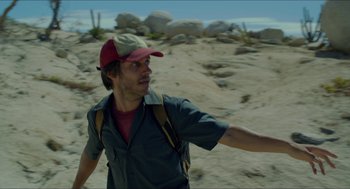 Movie still from “Desierto” (2015), directed by Jonás Cuarón – A man in a hat and a backpack walking on the beach; Close Up shot, Low angle