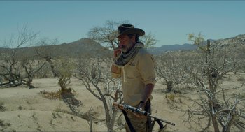 Movie still from “Desierto” (2015), directed by Jonás Cuarón – A man in a cowboy hat is standing in the desert with a rifle; Medium shot, Over the shoulder angle