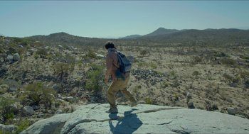 Movie still from “Desierto” (2015), directed by Jonás Cuarón – A man with a backpack is climbing a rock; Wide shot, Low angle