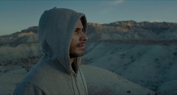 Movie still from “Desierto” (2015), directed by Jonás Cuarón – A man wearing a hooded sweatshirt standing on top of a hill; Close Up shot, High angle