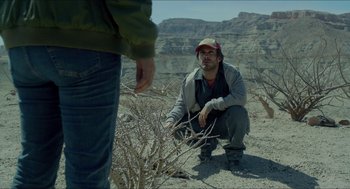 Movie still from “Desierto” (2015), directed by Jonás Cuarón – A man kneeling down in the desert looking at another man; Medium shot, Low angle