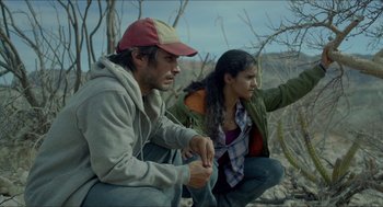 Movie still from “Desierto” (2015), directed by Jonás Cuarón – A man and a woman sitting on the ground near a tree; Medium shot, Low angle
