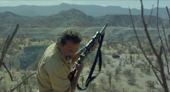 Movie still from “Desierto” (2015), directed by Jonás Cuarón – A man holding a rifle while standing on top of a hill; Medium shot, Low angle