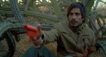 Movie still from “Desierto” (2015), directed by Jonás Cuarón – A man holding a gun while sitting in the woods; Close Up shot, High angle