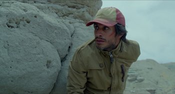 Movie still from “Desierto” (2015), directed by Jonás Cuarón – A man wearing a hat sitting in front of a cliff; Close Up shot, High angle