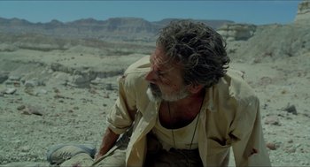 Movie still from “Desierto” (2015), directed by Jonás Cuarón – A man sitting on the ground in the desert; Medium shot, Over the shoulder angle