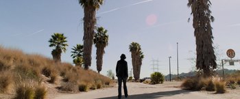 Movie still from “Destroyer” (2018), directed by Karyn Kusama – A person standing on the side of a road near some palm trees; Extreme Wide shot, Low angle