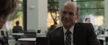 Movie still from “Destroyer” (2018), directed by Karyn Kusama – An older man wearing a suit and tie smiling; Close Up shot, Over the shoulder angle