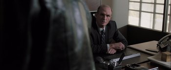 Movie still from “Destroyer” (2018), directed by Karyn Kusama – A man in a suit and tie sitting at a computer desk; Close Up shot, Over the shoulder angle