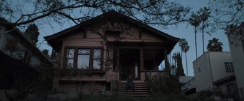 Movie still from “Destroyer” (2018), directed by Karyn Kusama – A person sitting on the steps of a house; Wide shot, Low angle