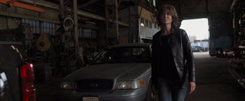 Movie still from “Destroyer” (2018), directed by Karyn Kusama – A woman standing in front of a car in a garage; Medium shot, Low angle
