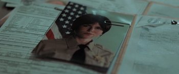 Movie still from “Destroyer” (2018), directed by Karyn Kusama – A picture of a woman in a police uniform with an american flag behind it; Extreme Close Up shot, Overhead angle