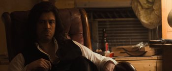 Movie still from “Destroyer” (2018), directed by Karyn Kusama – A man sitting in a leather chair with his legs crossed; Close Up shot, Low angle