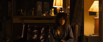 Movie still from “Destroyer” (2018), directed by Karyn Kusama – A woman sitting on top of a couch in a living room; Medium shot, Over the shoulder angle