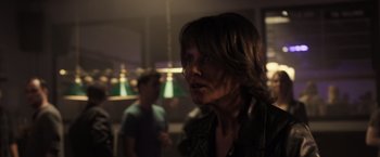 Movie still from “Destroyer” (2018), directed by Karyn Kusama – A woman with long hair and glasses looking at the camera with a man in the background; Close Up shot, Over the shoulder angle