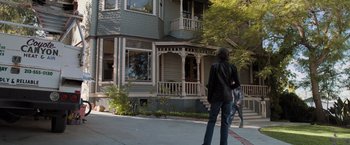 Movie still from “Destroyer” (2018), directed by Karyn Kusama – A person walking down the street in front of a house; Wide shot, Low angle