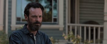Movie still from “Destroyer” (2018), directed by Karyn Kusama – A man with a beard is sitting in front of a building; Close Up shot, Over the shoulder angle