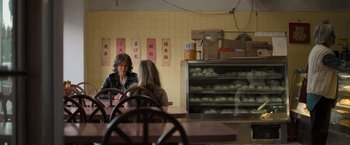 Movie still from “Destroyer” (2018), directed by Karyn Kusama – Two women sitting at a table in front of a display of buns; Medium shot, Over the shoulder angle