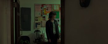 Movie still from “Destroyer” (2018), directed by Karyn Kusama – A person standing in a room with a bunch of papers on the wall; Medium shot, Over the shoulder angle
