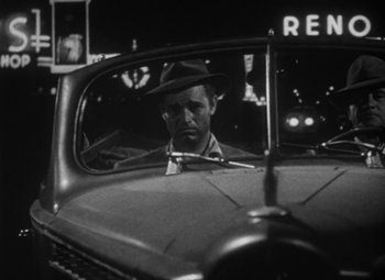 Movie still from “Detour” (1945), directed by Edgar G. Ulmer – A black and white photo of a man in a hat in the back of a car; Close Up shot, Low angle