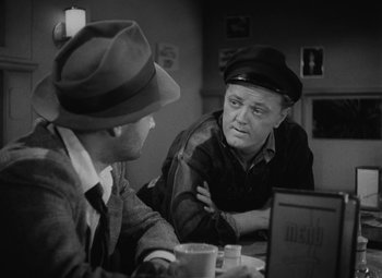 Movie still from “Detour” (1945), directed by Edgar G. Ulmer – Two men are sitting at a table and one of the men has a hat on; Medium shot, Over the shoulder angle