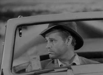 Movie still from “Detour” (1945), directed by Edgar G. Ulmer – A black and white photo of a man in a hat looking out of the window of a car; Close Up shot, Over the shoulder angle