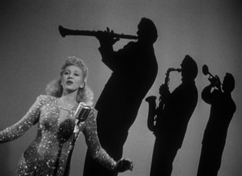 Movie still from “Detour” (1945), directed by Edgar G. Ulmer – A black - and - white photo of a woman and a saxophone player; Wide shot, Low angle