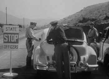 Movie still from “Detour” (1945), directed by Edgar G. Ulmer – A black - and - white photo of three men standing next to a car; Wide shot, Low angle