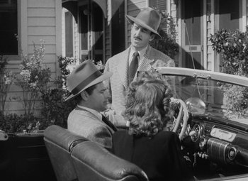 Movie still from “Detour” (1945), directed by Edgar G. Ulmer – Two men and a woman sitting in the back of an old car; Medium shot, High angle
