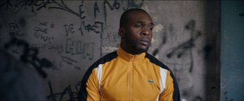 Movie still from “Dheepan” (2015), directed by Jacques Audiard – A man in a yellow and white jacket is standing in front of a wall; Medium shot, High angle