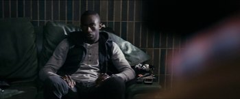 Movie still from “Dheepan” (2015), directed by Jacques Audiard – A man sitting on a couch with a cell phone; Medium shot, High angle